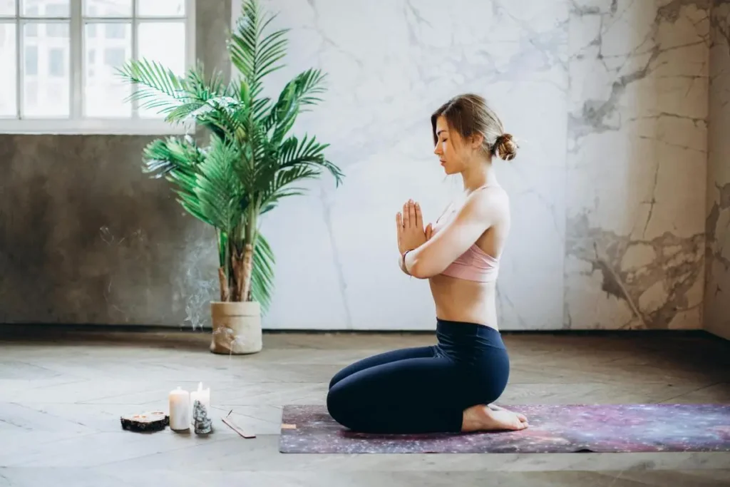 Femme méditant en position assise sur un tapis de yoga avec des bougies et de l'encens, pratiquant la gratitude en intérieur.