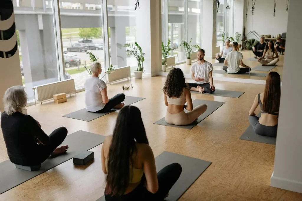 Cours collectif de yoga guidé par un enseignant, pratiqué dans une salle lumineuse avec vue extérieure.
