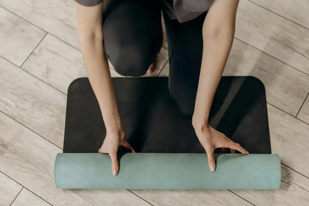 Personne déroulant un tapis de yoga sur un sol en bois, prête à commencer une séance.