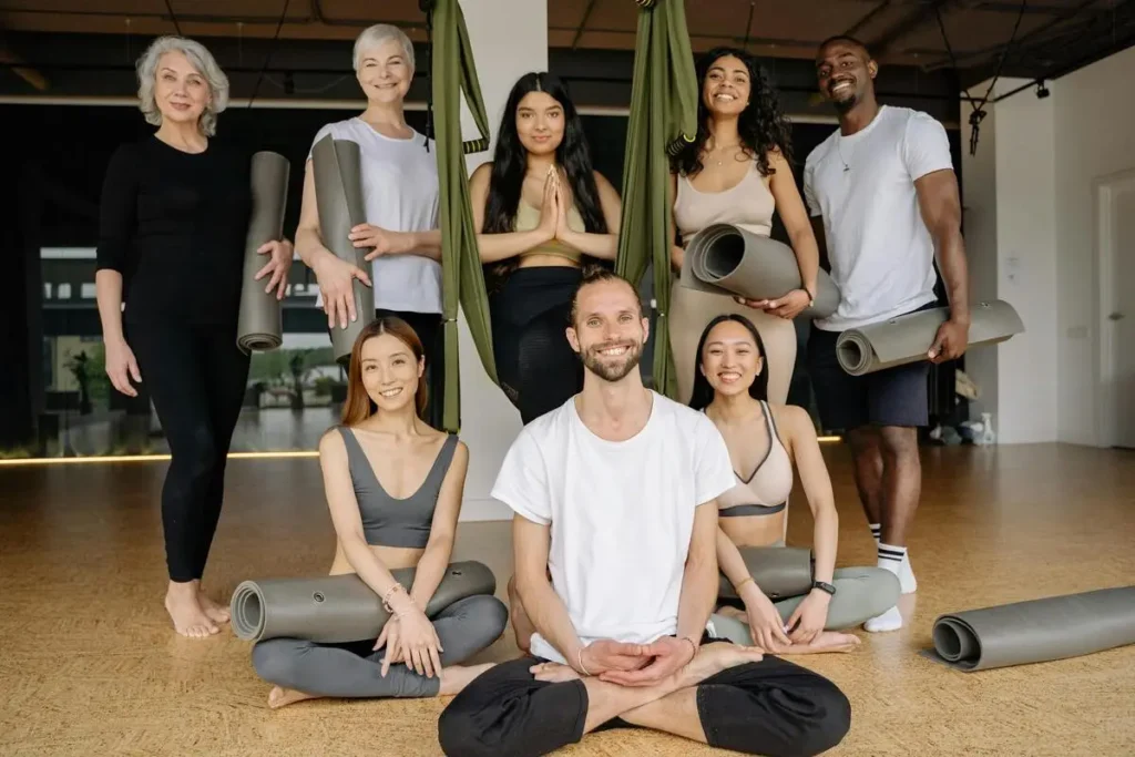 Professeur de yoga entouré de ses élèves souriants dans une salle de yoga.