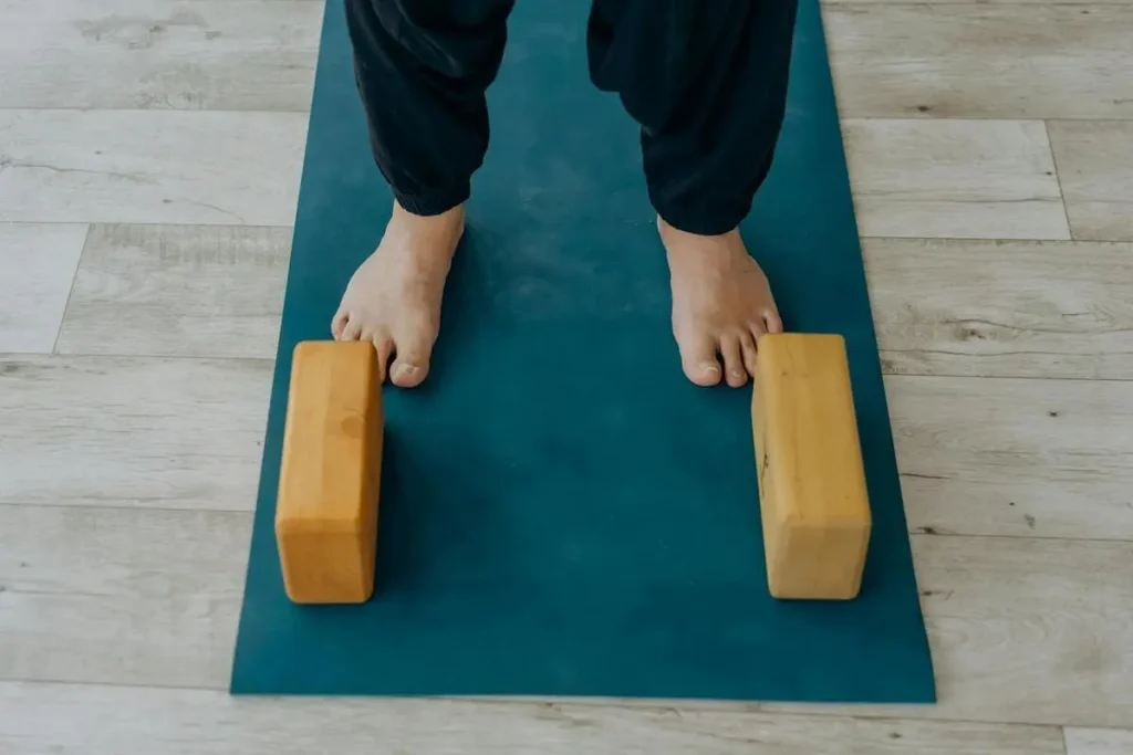 Pieds nus sur un tapis de yoga avec deux briques en bois, illustrant la posture de départ d’un exercice de yoga pour débutant.