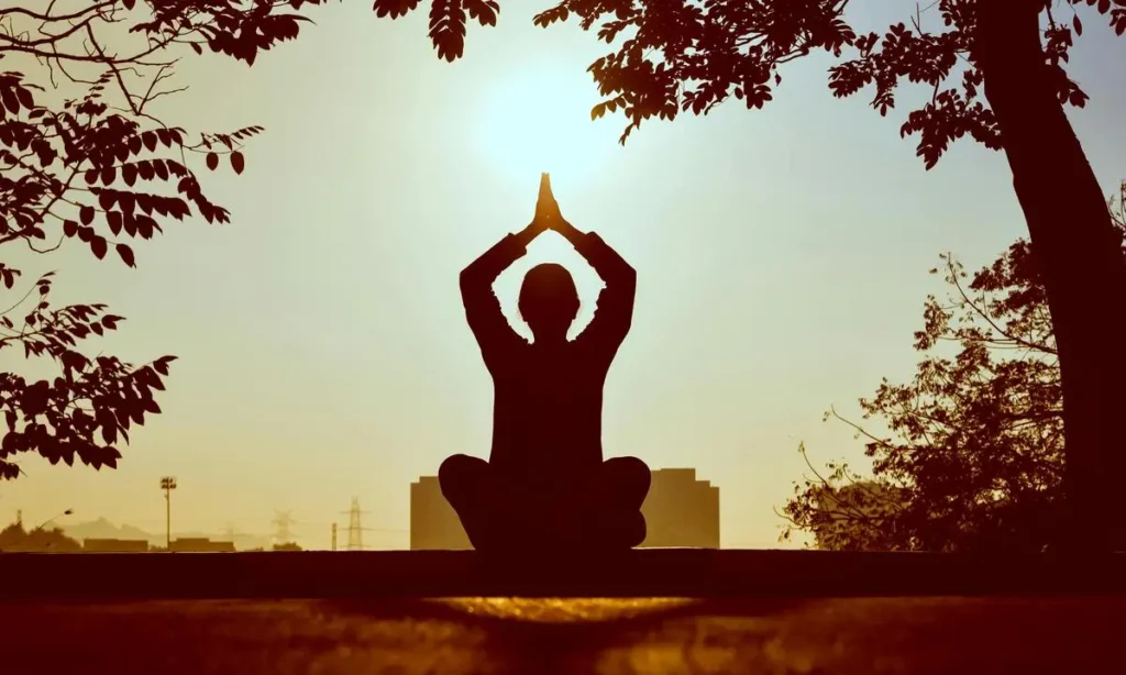 Personne méditant au lever du soleil en posture de yoga.
