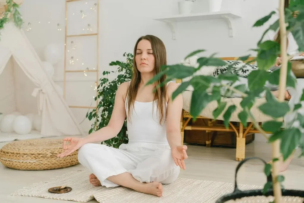 Femme en blanc méditant en position assise dans un intérieur lumineux et végétalisé